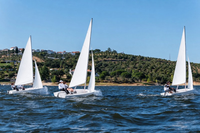 Três embarcações à vela a navegar nas águas de uma albufeira
